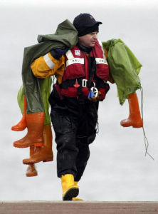 在英格蘭西北部莫克姆灣海灘，一名救援人員將找到的遇難者的防水服送上岸。