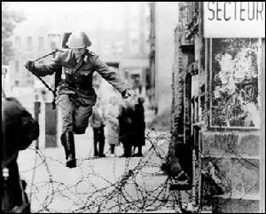 19歲的東德士兵康拉德•舒曼頭戴鋼盔、肩背長槍大步躍過鐵蒺藜樊籬。