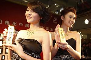 （圖）兩名工作人員正在首發儀式上展示1千克重的財富金條