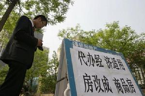 某房產中介公司的員工在代辦“經轉商”手續的廣告牌前等候顧客。