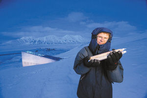 “斯瓦爾巴特全球物種庫”發起人卡里·福勒手持兩個豌豆瓶。在他身後就是挪威斯匹次卑爾根島全球物種庫。